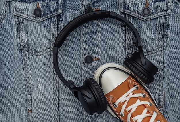 Youth, hipster clothing and accessories. Sneaker with headphones on jeans jacket background. Top view. Flat lay