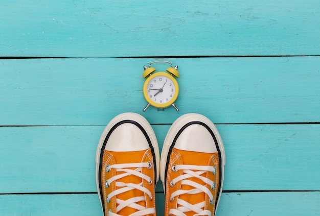 Youth retro sneakers and mini alarm clock on a blue wooden background.