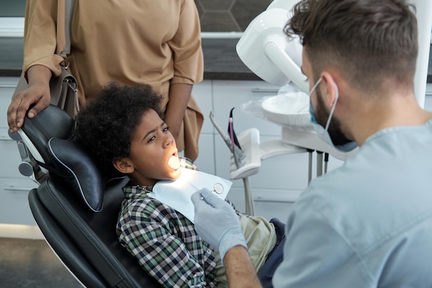 Photo youthful boy with open mouth looking at dentist before oral checkup