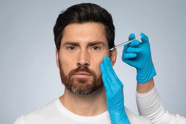 Youthful enhancement handsome middle aged man receiving facial beauty injections grey studio