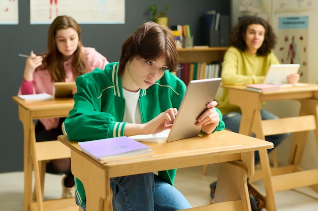 Youthful female student in casualwear looking at tablet screen at lesson