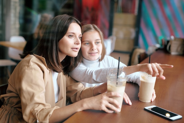 Youthful girl pointing forwards while showing her mom something curious