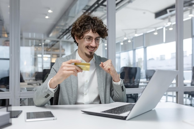 A youthful male entrepreneur with curly hair beaming as he confidently holds a credit card in a