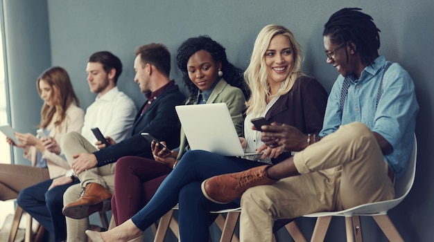 Youve been shortlisted but who will get the job Shot of a group of businesspeople using different wireless devices while waiting in line for an interview