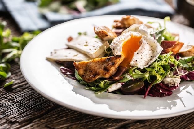 Buonissima l'estate fresca come l'insalata di lattuga fatta di vari tipi di foglie servita nel piatto con pezzi di delizioso formaggio di pecora, petto di pollo croccante alla griglia e uovo che cola condito.