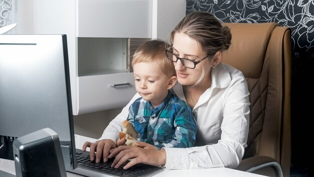 Yung zakenvrouw zit met kind thuis en werkt op de computer vanuit kantoor aan huis.