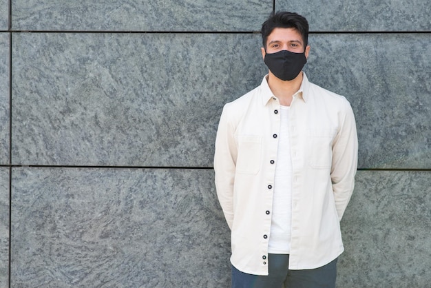Ygiovane uomo mascherato in piedi vicino a un muro covid e concetto di coronavirus
