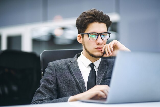 Zaakvoerder in glazen werkt op zijn laptop op kantoor. Jonge freelancer die vanaf een laptop werkt.