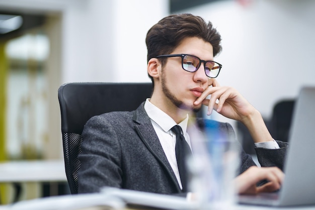 Zaakvoerder in glazen werkt op zijn laptop op kantoor. Jonge freelancer die vanaf een laptop werkt.