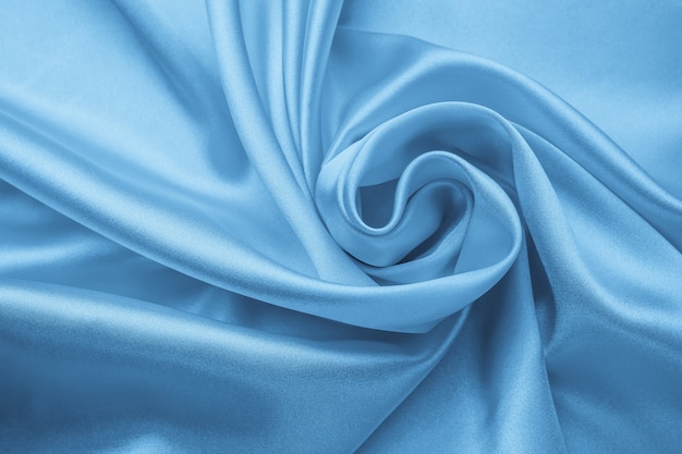 Zacht golvend pastel materiaal, blauwe glanzende textuur van textiel. Satijnen plooien, golvenpatroon. Zijdeachtige achtergrond met rondingen, luxe mode. Gevouwen doek, behang.