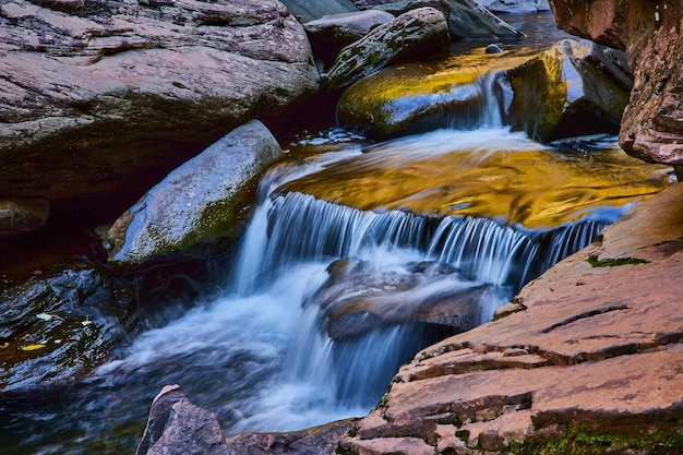 Zacht warm licht over prachtige kleine trapsgewijze waterval omgeven door gladde rotsen