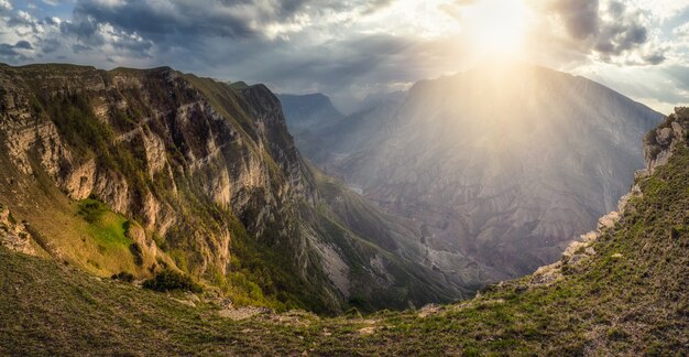 Zachte focus. Dramatisch landschap met de heldere stralen van de zon door de wolken boven de bergen. Schilderachtig Kaukasisch groen landschap met bergrivier in diepe kloof onder bewolkte hemel. Dagestan