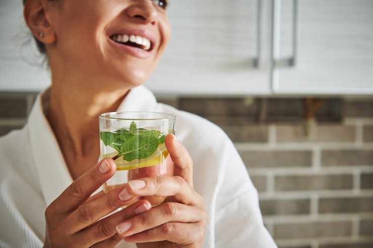 Foto zachte focus op een glas met water, munt en schijfje citroen in de handen van een wazige latijns-amerikaanse vrouw die lacht met een mooie brede glimlach