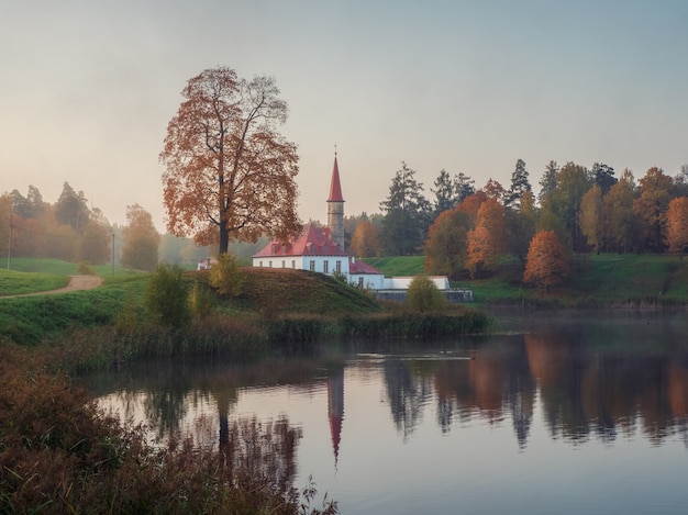 Zachte focus. Zonnig herfst ochtend landschap. Een helder mistig herfstlandschap met gouden bomen bij de vijver en een oud paleis. Gatchina. Rusland.