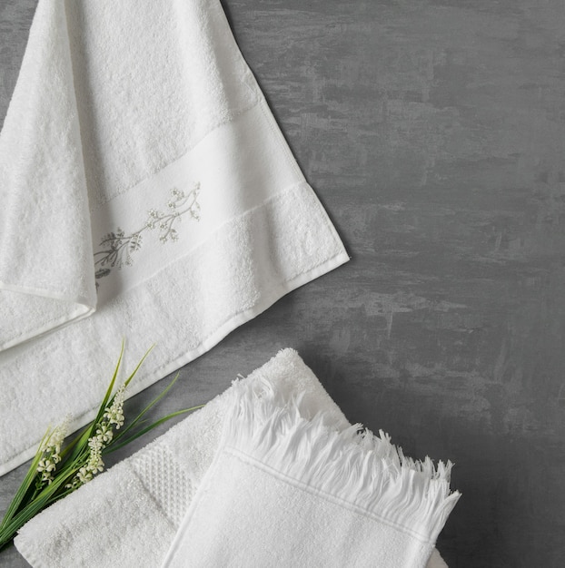Zachte handdoek met een bloem op een grijze decoratieve stucwerkachtergrond. bovenaanzicht, geïsoleerd