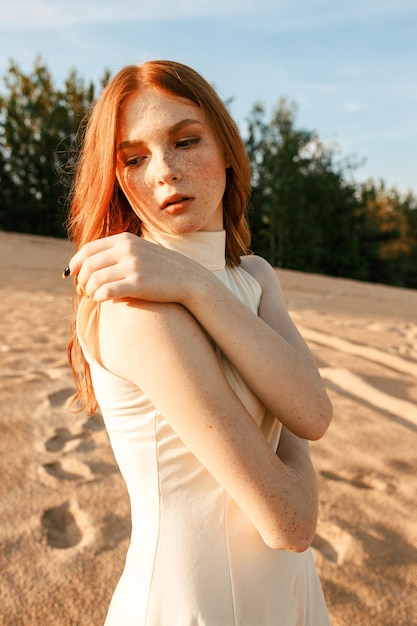 Zachte vrouw met natuurlijke lang rood haar en sproeten staande op zandstrand op zonnige dag in de zomer