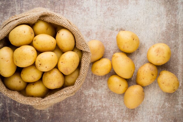 Zak met verse rauwe aardappelen op houten achtergrond, bovenaanzicht.