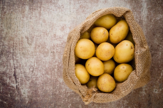 Zak met verse rauwe aardappelen op houten achtergrond, bovenaanzicht.