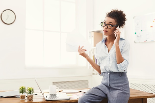 Zakelijk bellen. Serieuze ceo zakenvrouw praten op mobiel in moderne kantoren, zittend op het bureau, kopieer ruimte