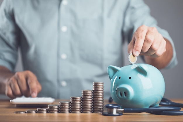 Foto zakelijk financieel en geld check-up idee controleer de gezondheid van financiële planning voor gezondheidsconcept man voegt munt toe aan blauw spaarvarken en toenemende munt gestapeld op tafel