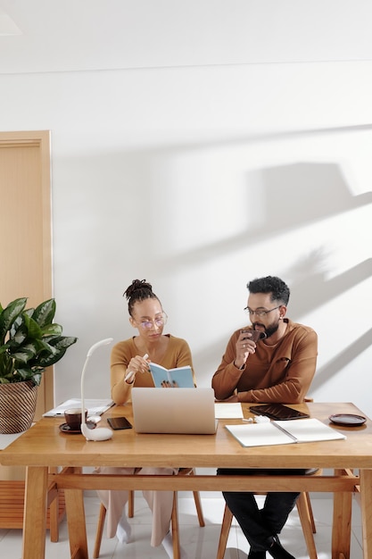 Zakelijk koppel dat koffie drinkt, planner controleert en plannen voor de dag bespreekt wanneer ze aan het bureau zitten