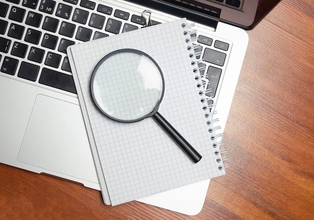 Foto zakelijk notitieboekje met laptop en vergrootglas aan bureau hoge kwaliteit foto