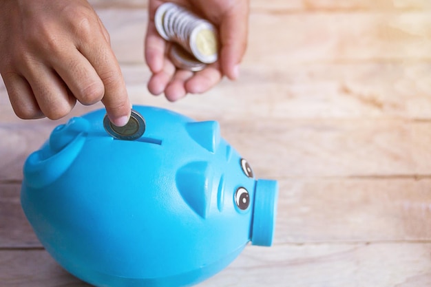 Foto zakelijk of financieel besparingsconcept met hand die munt in blauw spaarvarken stopt