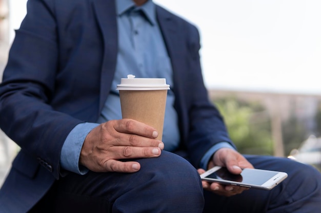 Zakelijk onderwijs technologie communicatie en mensen concept creatieve man met smartphone koffie drinken uit papieren beker en zittend op straatbankje in de stad