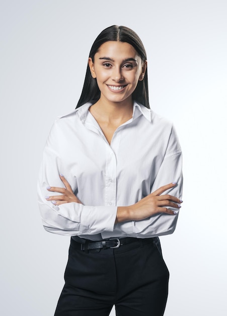 Zakelijk succesconcept met geïsoleerde jonge lachende vrouw gevouwen haar handen in wit overhemd zwarte broek op abstracte lichte lege achtergrond
