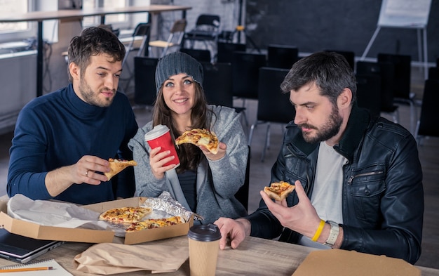 Zakelijk team dat pizza eet en drinkt op kantoor Vrouw geeft pizza aan camera