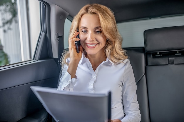 Zakelijk telefoontje. Blonde vrouw praten over een telefoon in een auto en op zoek betrokken