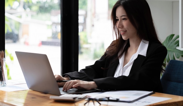 Zakelijke aziatische vrouw die laptop gebruikt om wiskunde te financieren op houten bureau in kantoor, belasting, boekhouding, financieel concept