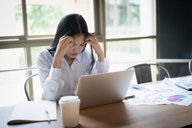 Zakelijke aziatische vrouw voelt zich moe en houdt het hoofd serieus en werkt met laptop Depressie aziatische vrouw die hard werkt