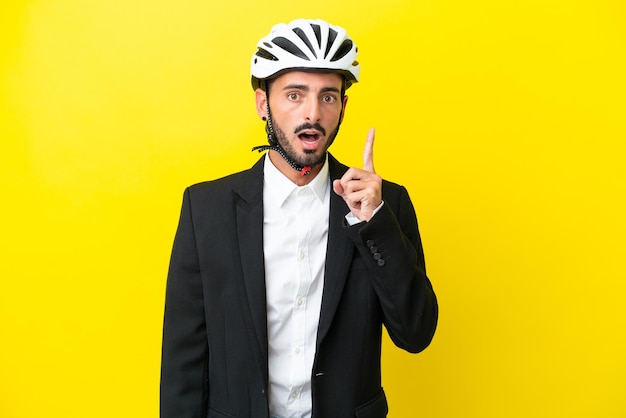 Zakelijke blanke man met een fietshelm geïsoleerd op een gele achtergrond, denkend aan een idee met de vinger omhoog