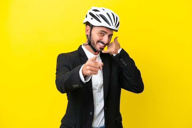 Zakelijke blanke man met een fietshelm geïsoleerd op een gele achtergrond die een telefoongebaar maakt en naar voren wijst