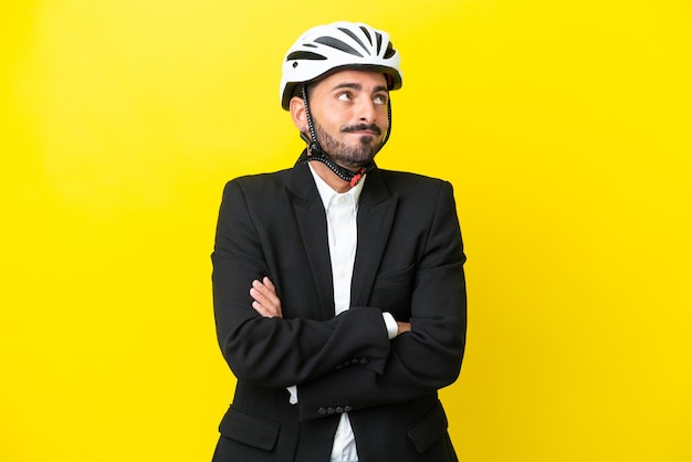 Zakelijke blanke man met een fietshelm geïsoleerd op een gele achtergrond die twijfels maakt terwijl hij de schouders opheft