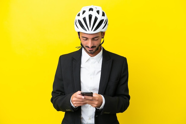 Zakelijke blanke man met een fietshelm geïsoleerd op gele achtergrond die een bericht verzendt met de mobiel