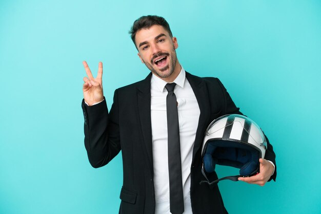 Zakelijke blanke man met motorhelm geïsoleerd op blauwe achtergrond glimlachend en overwinningsteken tonen