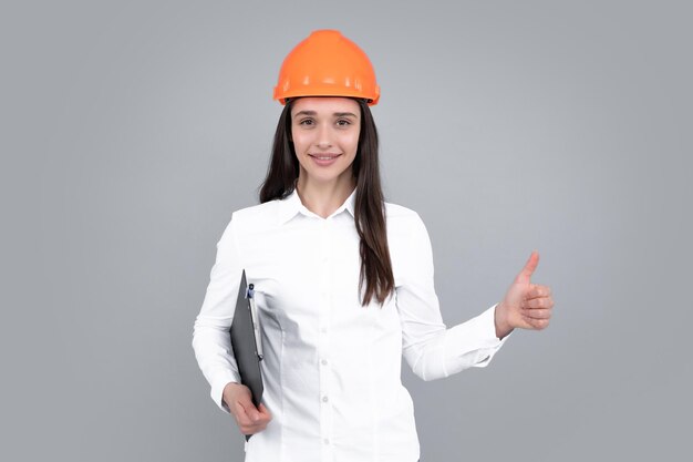 Zakelijke bouwer vrouw met klembord portret op grijs Portret van werkneemster met thumbs up in hardhat helm