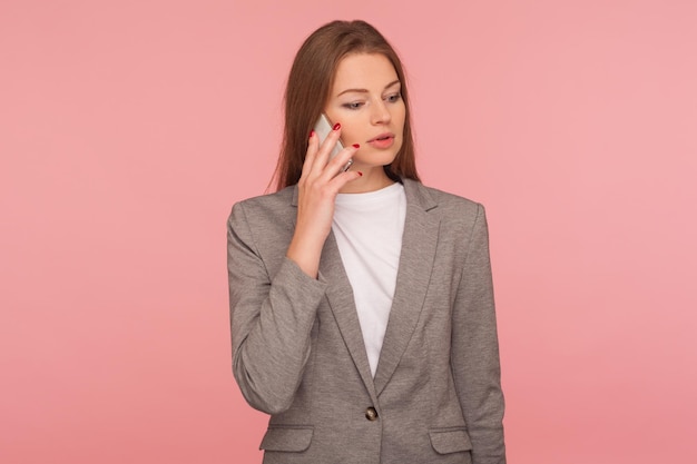 Zakelijke cellulaire, mobiele communicatie. Portret van een serieuze elegante damebaas in een stijlvol colbert die op de mobiele telefoon praat, zakelijke problemen oplost, de klant raadpleegt. studio-opname, roze achtergrond