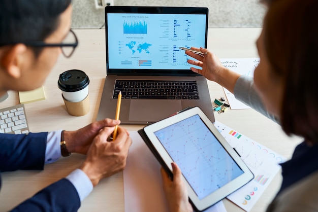 Zakelijke collega's die de activiteit van websitebezoekers bespreken tijdens de vergadering en wijzen op het laptopscherm met grafieken en diagrammen