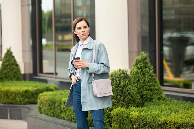 Zakelijke dame in trenchcoat drinkt onderweg koffie in de stad Lifestyle