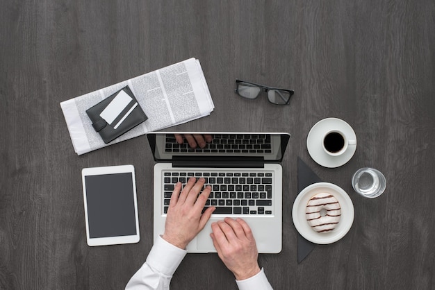 Zakelijke desktop met laptop, tablet, krant, koffie en een donut plat gelegd