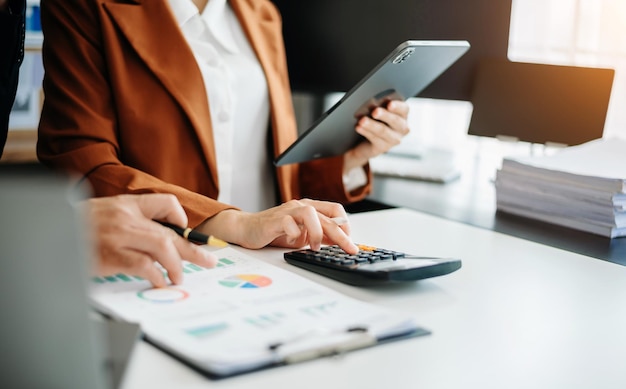 Zakelijke documenten op kantoortafel met slimme telefoon en rekenmachine digitale tablet en grafiekbedrijf met sociaal netwerkdiagram en twee collega's die gegevens bespreken die in de officexAxA werken