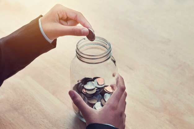 Zakelijke hand munten aanbrengend glazen pot voor het opslaan van geld boekhoudkundige concept op tafel