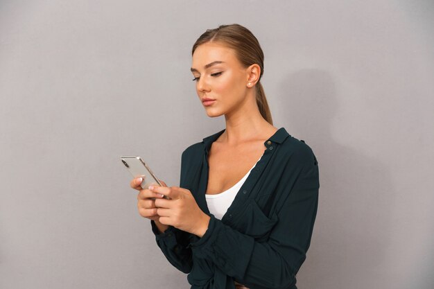 Zakelijke jonge vrouw poseren geïsoleerd over grijze muur achtergrond met behulp van mobiele telefoon.