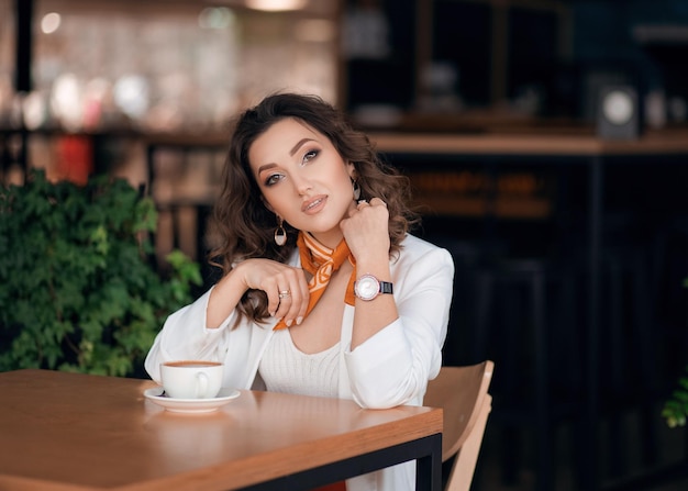 Zakelijke jonge vrouw zit aan een tafel in een café koffie te drinken, ze draagt een witte jas