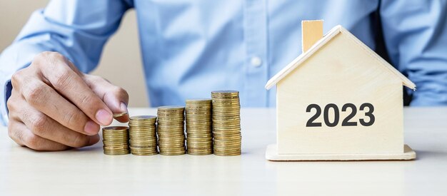 Zakelijke man hand gouden munt zetten groeiende geld trappen met 2023 houten huis gelukkig nieuwjaar zakelijke investeringen pensioen planning financiën opslaan en nieuwe u concepten