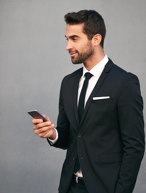 Zakelijke man telefoon en glimlach met vertrouwen idee en sociale media pauze in de studio pak corporate en executive mode met mobiele netwerken werknemer en professionele stijl met grijze achtergrond