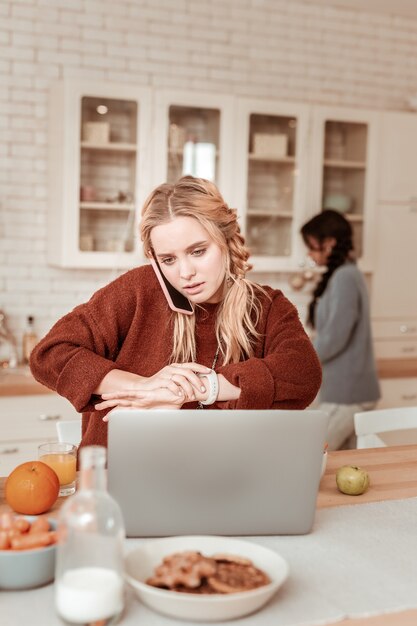 Zakelijke momenten. blond meisje geconcentreerd bezig met de keukentafel en praten over werk op mobiele telefoon